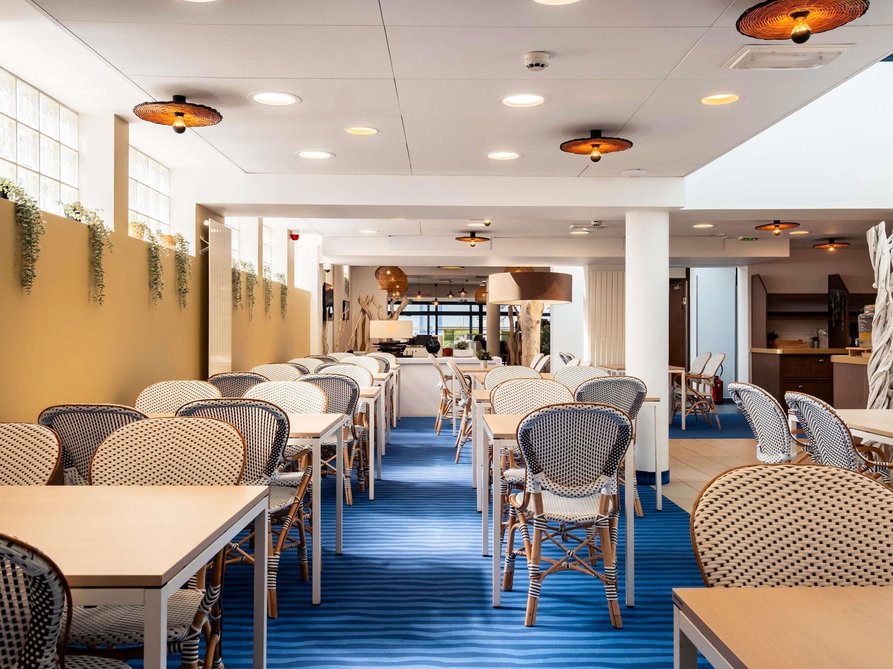 Uma área de refeições de hotel com cadeiras de vime, mesas e luminárias no teto.