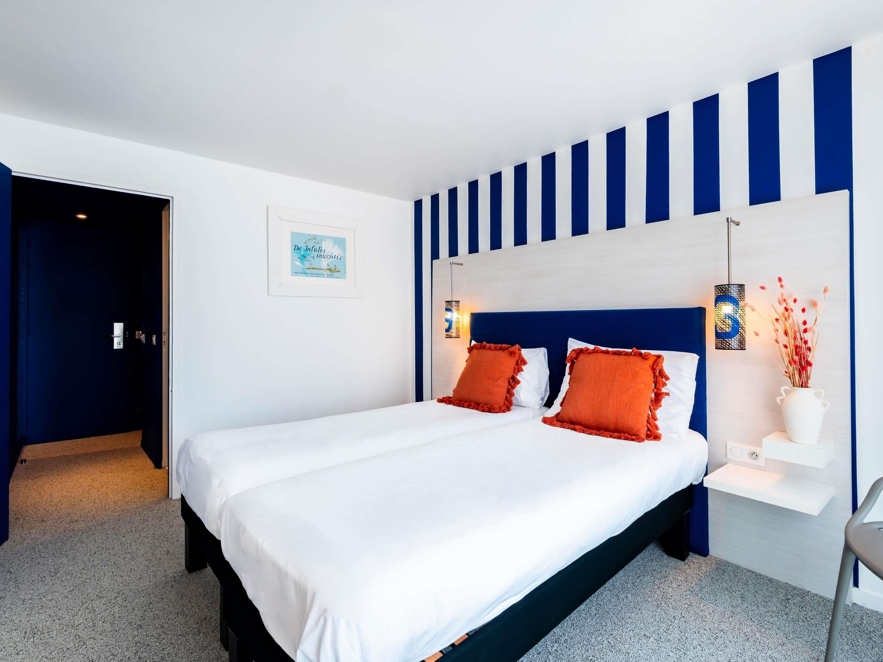 A modern hotel room with a large bed, a nightstand, a wall-mounted lamp, and a framed picture.