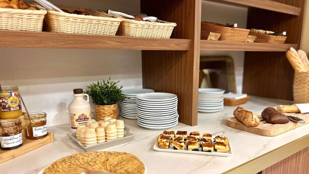 A breakfast buffet with various food items, wicker baskets, and stacked plates. - ibis Styles Quiberon Centre (Quiberon)