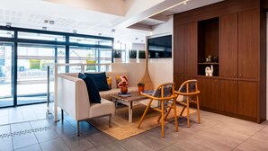 A modern hotel lobby with a sofa, chairs, a coffee table, a TV, and wooden cabinets. - ibis Styles Quiberon Centre (Quiberon)