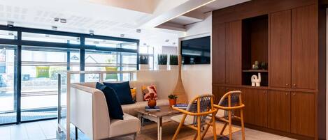 A modern hotel lobby with a sofa, chairs, a coffee table, a TV, and wooden cabinets.