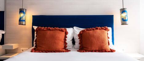 Habitación de hotel con pared a rayas, cabecero azul, dos almohadas rojas y dos lámparas fijadas a la pared.