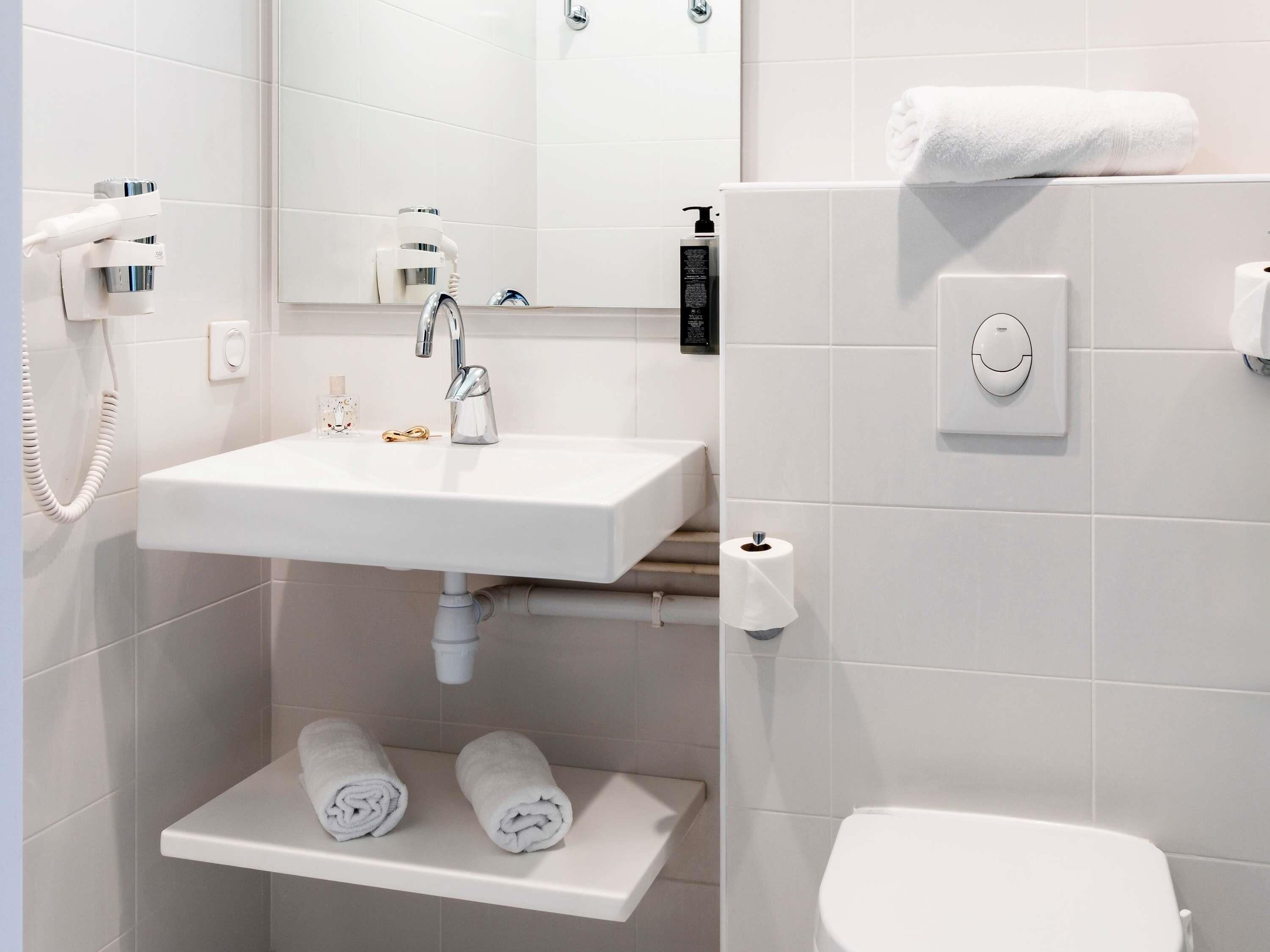 Une salle de bain moderne avec un lavabo blanc, un miroir, un porte-serviettes et des toilettes.