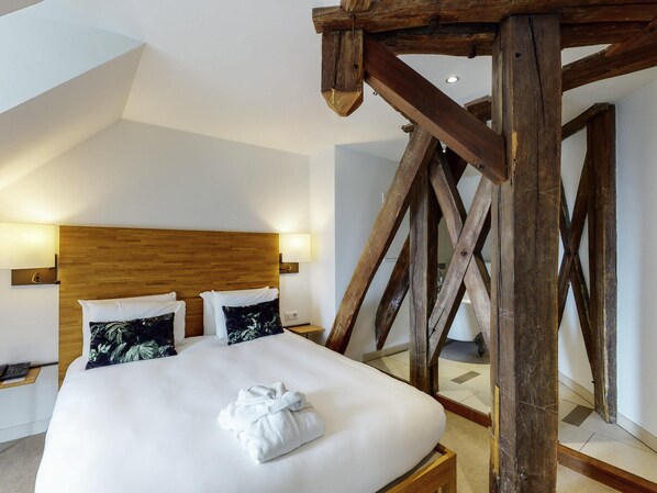 Una habitación de hotel con estructura de techo de madera, una cama con ropa de cama blanca y dos lámparas fijadas a la pared.