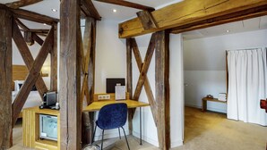 A rustic room with exposed wooden beams, a desk with a computer, a blue chair, and a small trash can.