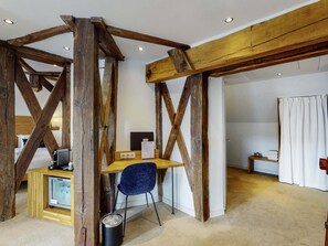 Una habitación rústica con vigas de madera a la vista, un escritorio con ordenador, una silla azul y un cubo de basura pequeño.