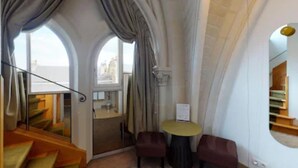 A room with a curved ceiling, a small table with chairs, a window with curtains, and a staircase.
