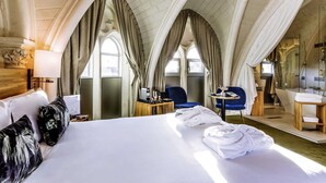 A hotel room with a large bed, a small table with a coffee maker, two chairs, and a bathroom with a bathtub and shower.