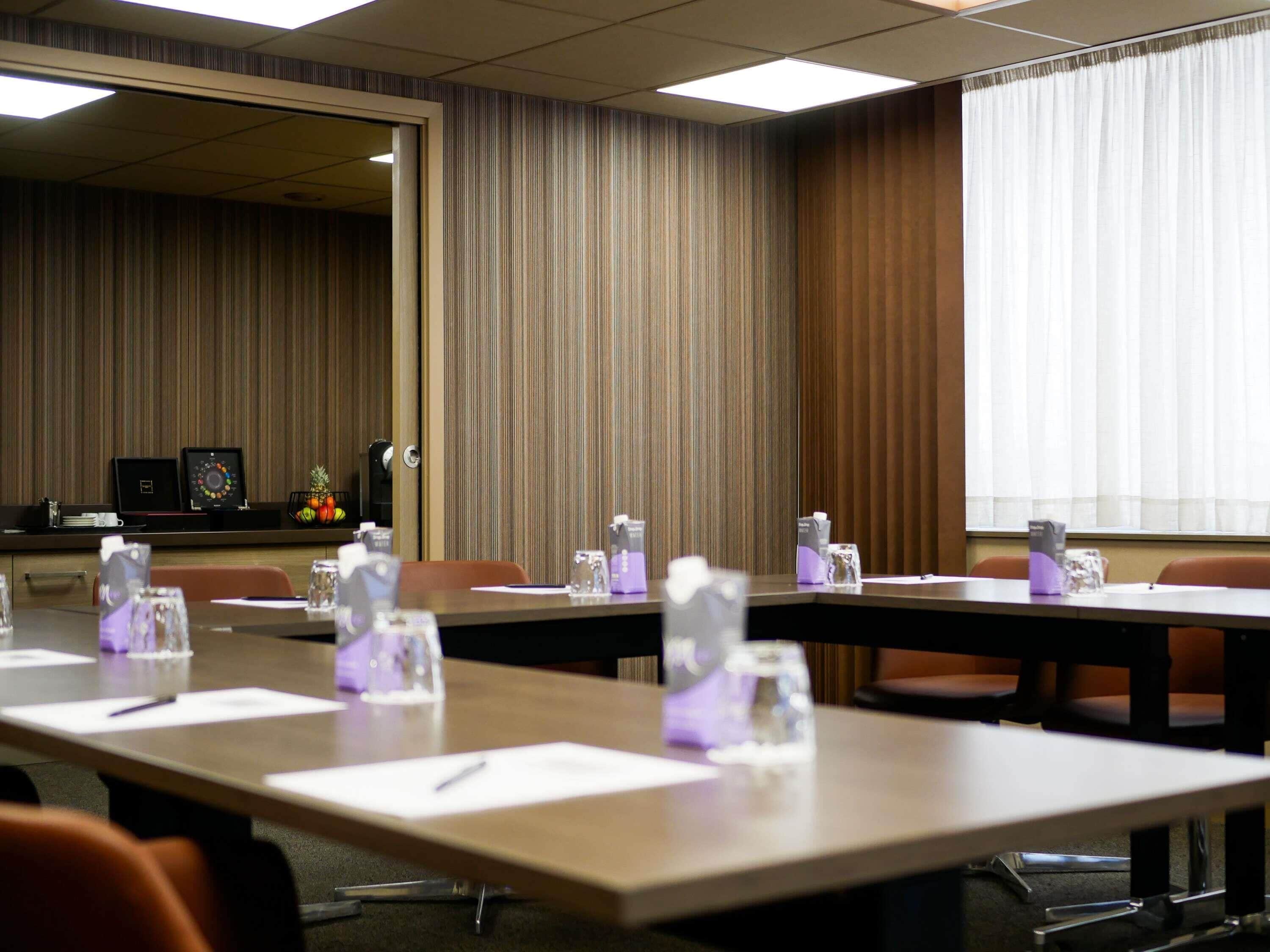 A conference room with long tables, chairs, and a large window with curtains.