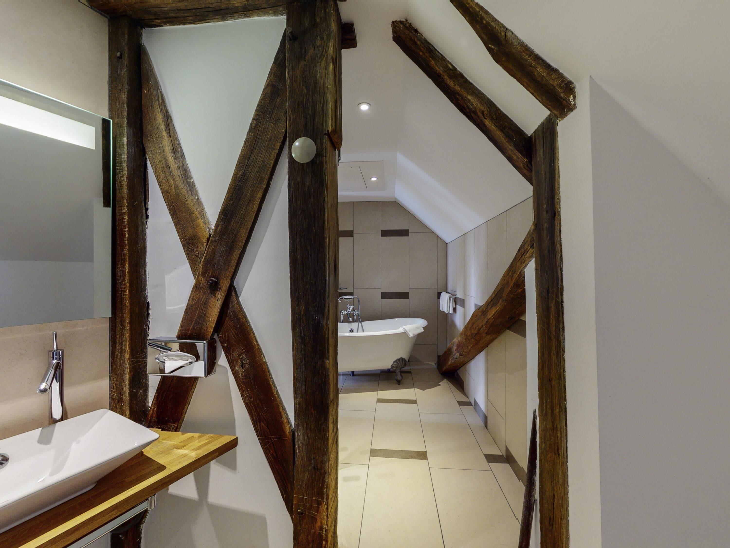 Une salle de bain moderne avec une structure en poutres apparentes, un lavabo et une baignoire.