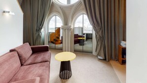 A modern interior with a large arched window, a pink sofa, a round table, and a view of a staircase.