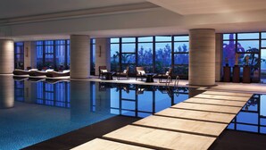 A modern indoor pool area with clear glass walls, wooden deck, and lounge chairs. - Sheraton Hefei Xinzhan Hotel (Hefei)