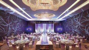 Un salón de banquetes con mesas redondas, sillas blancas y un pasillo central.