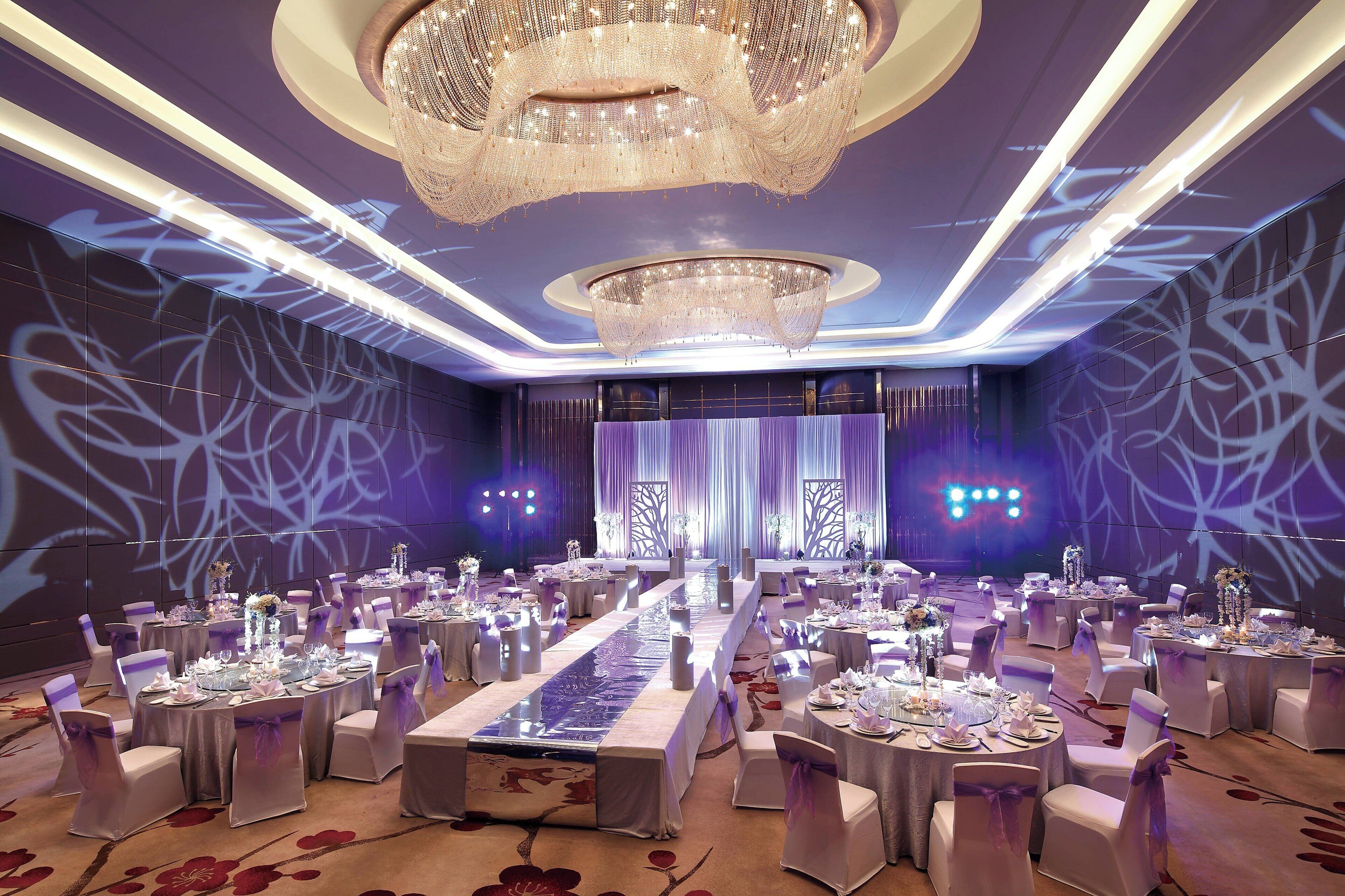 A banquet hall with round tables, white chairs, and a long table with a floral table runner.