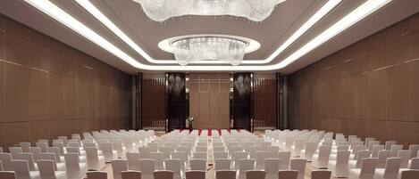 A spacious hall with rows of white chairs, a large chandelier, and a floral carpet.