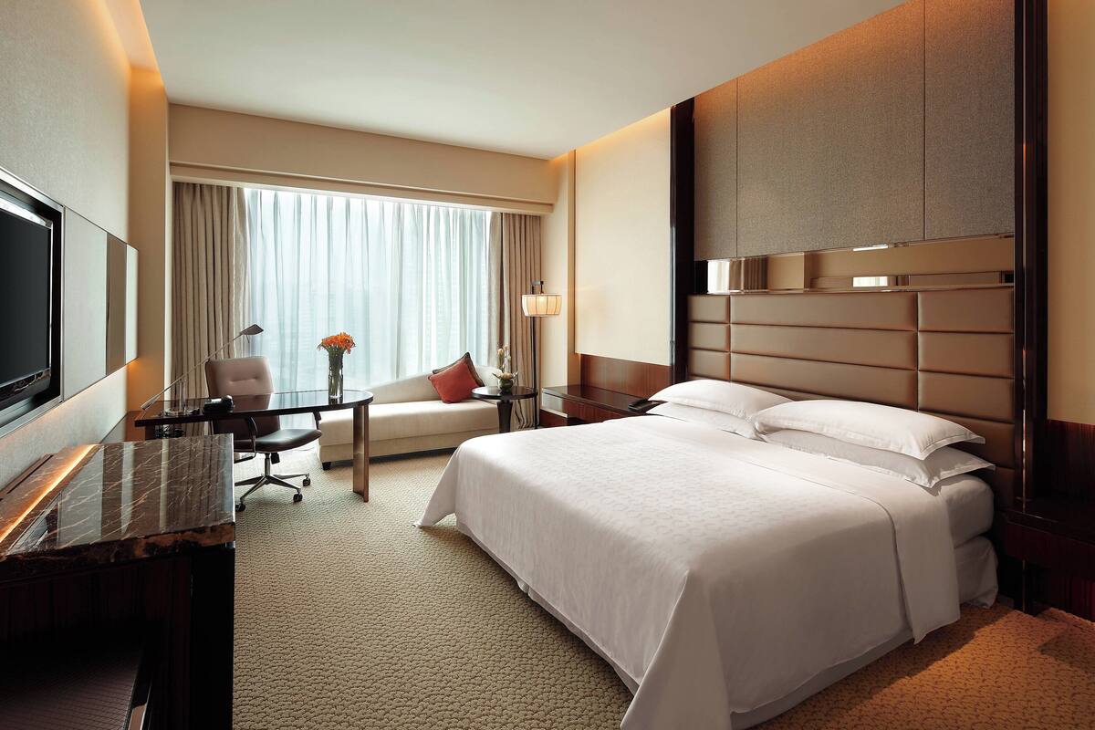 A hotel room with a large bed, a desk, a chair, a TV, and a window with curtains.