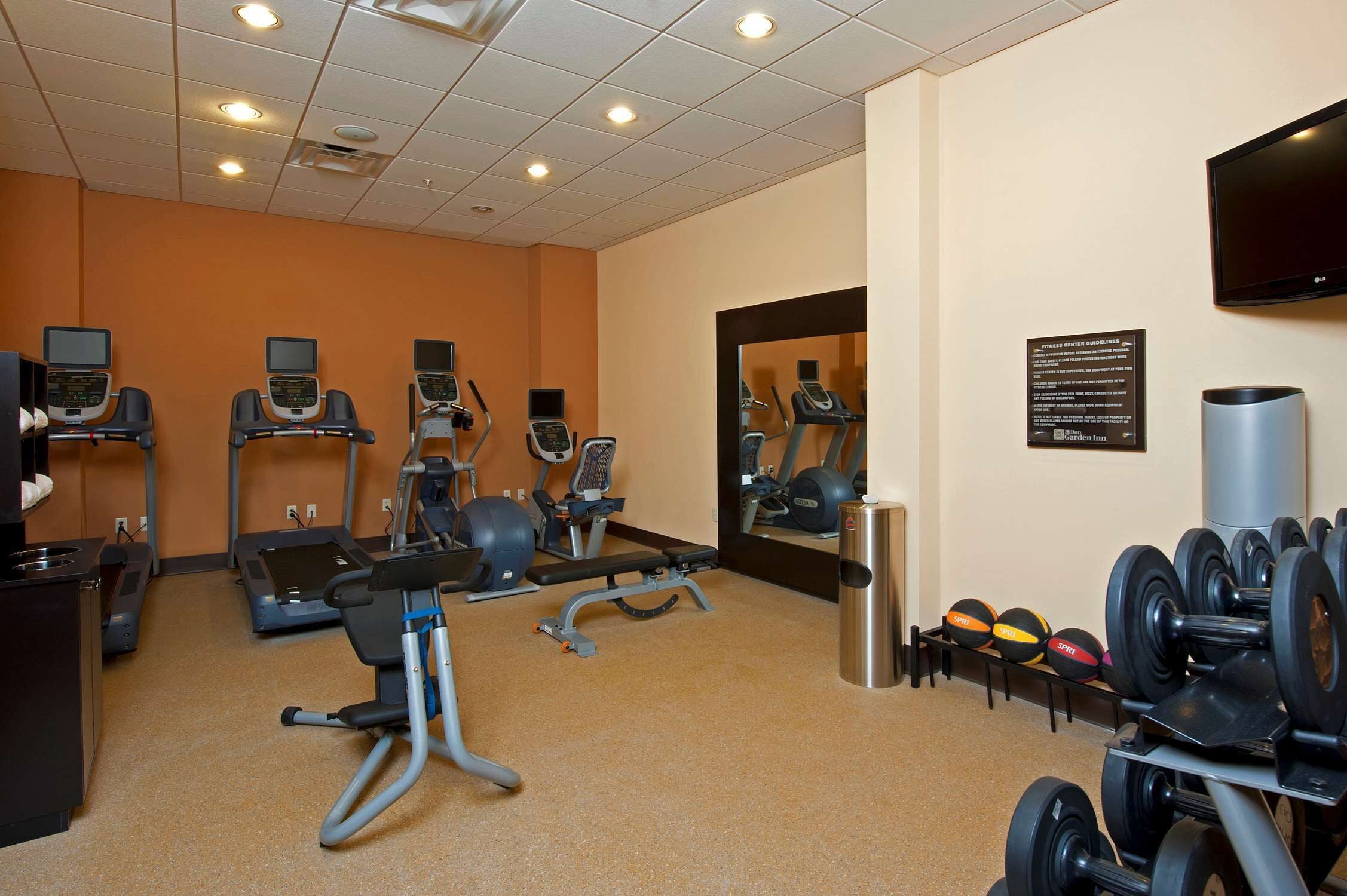 Une salle de sport équipée de tapis de course, de vélos elliptiques, d’un banc de développé couché et d’une série de haltères.