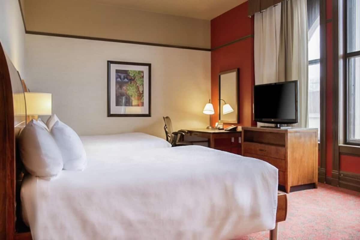 Una habitación de hotel con dos camas, un escritorio, un televisor y una ventana con cortinas.