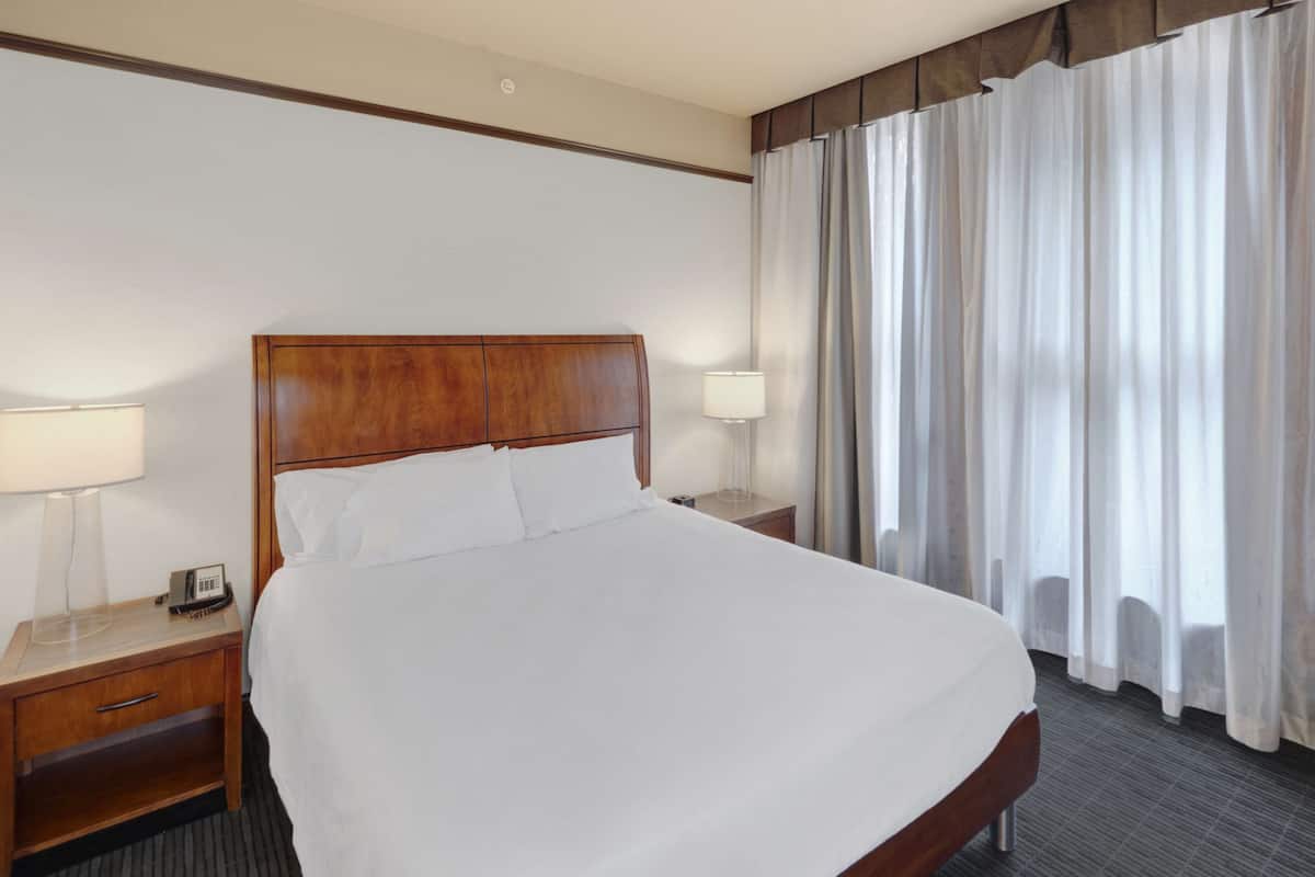 Habitación de hotel con una cama grande, dos mesitas de noche, una lámpara, un teléfono y una ventana con cortinas.