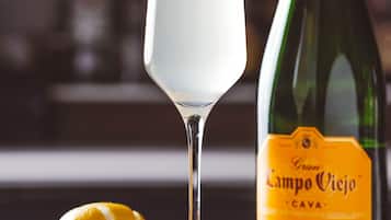 A glass of a clear beverage with a lemon slice garnish, a bottle labeled "Campo Viejo Cava," and a lemon half on a reflective surface.