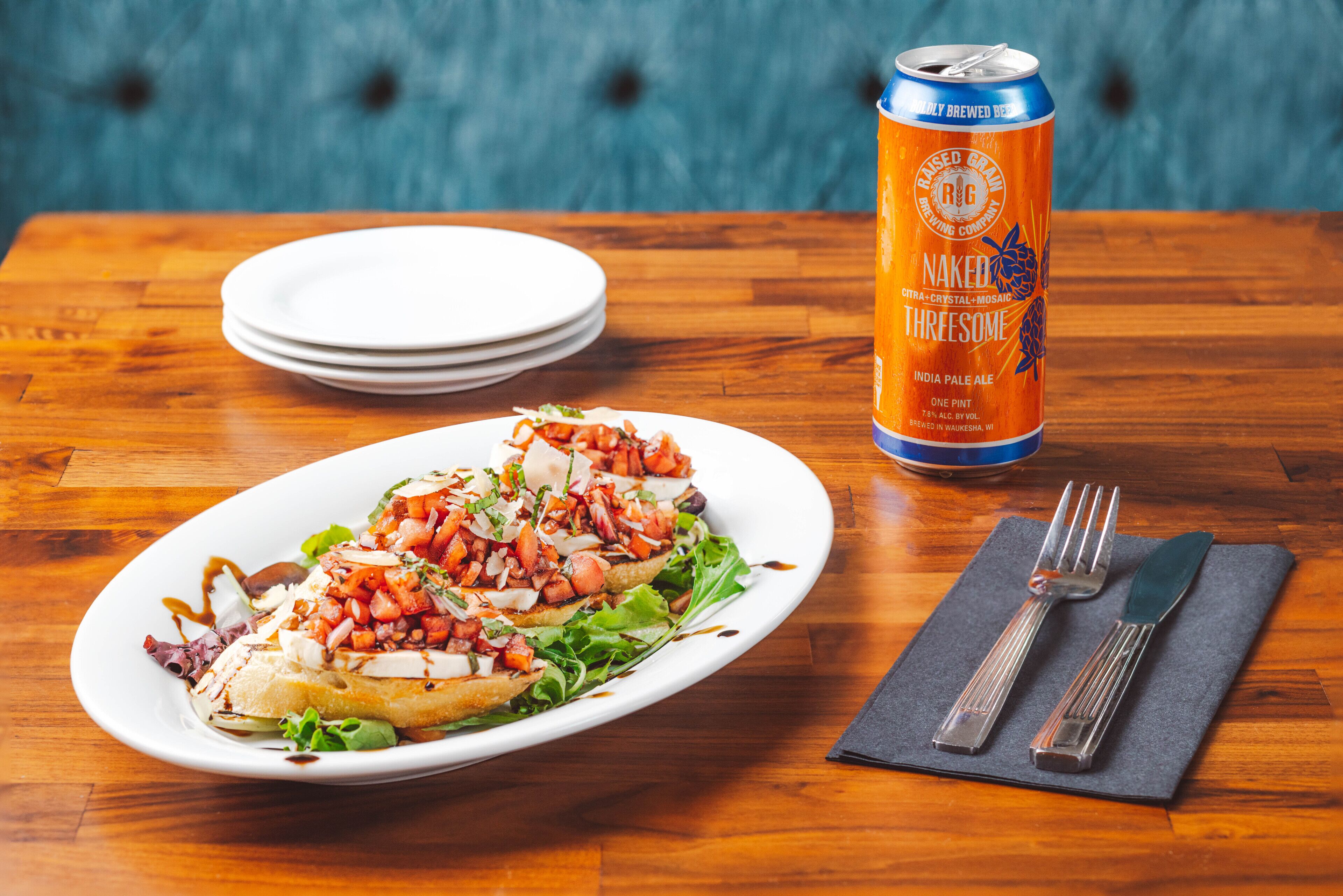 Prato de comida com uma lata de cerveja e talheres sobre uma mesa de madeira.