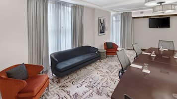 Ein Hotelzimmer mit einer Couch, einem Sessel und einem Konferenztisch mit Stühlen.