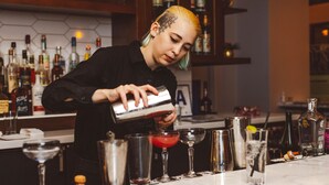 Um bartender preparando bebidas em um bar, com diversas garrafas e copos.