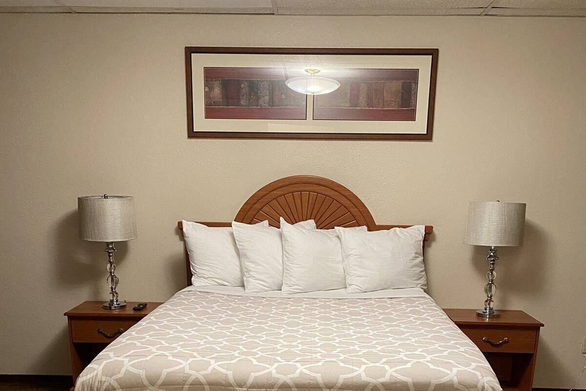 A neatly made bed with a patterned bedspread, two bedside lamps, and a framed picture on the wall above.