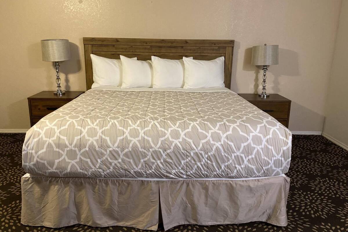 A neatly made bed with a patterned bedspread, two bedside tables with lamps, and a patterned carpet.
