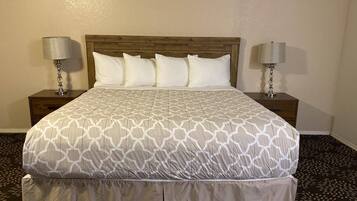 A neatly made bed with a patterned bedspread, two bedside tables with lamps, and a patterned carpet.