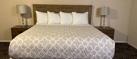 A neatly made bed with a patterned bedspread, two bedside tables with lamps, and a patterned carpet.
