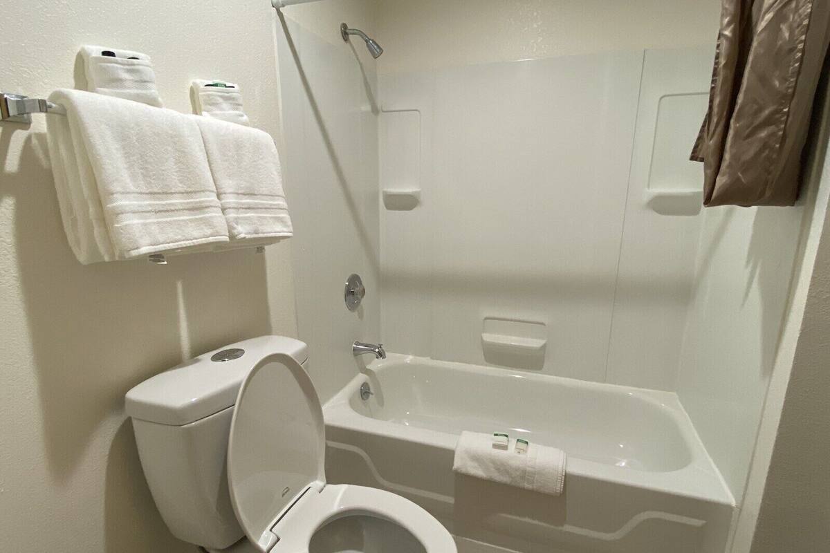 A bathroom with a toilet, a bathtub, and a shower. There are towels hanging on the wall.