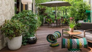 A cozy outdoor seating area with a sofa, chairs, and a table under a large umbrella. - Hotel Das Stue Berlin (Berlin)