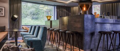 Un área de bar moderna con una barra alta, varios taburetes y una zona de estar con sofá y sillones.