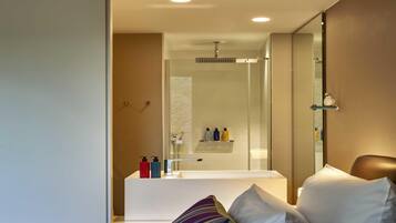 A modern bathroom with a glass shower enclosure, a white bathtub, and toiletries on a shelf.