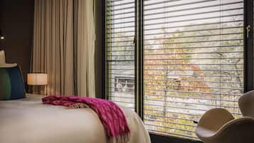 Une chambre d’hôtel avec un lit, une chaise, une fenêtre avec des stores et une lampe.