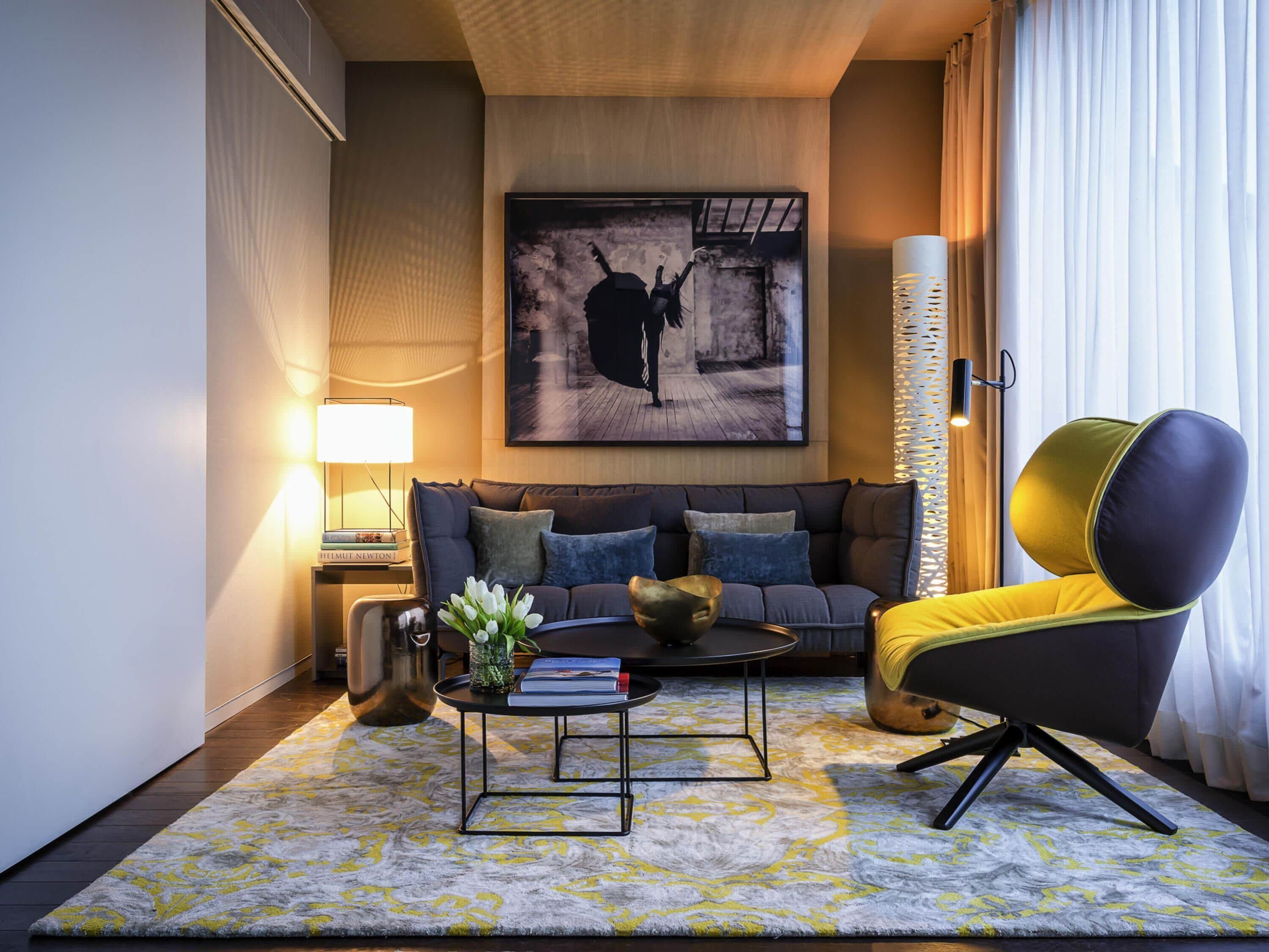 A modern living room with a sofa, coffee table, and a unique chair, featuring a painting on the wall and a lamp.