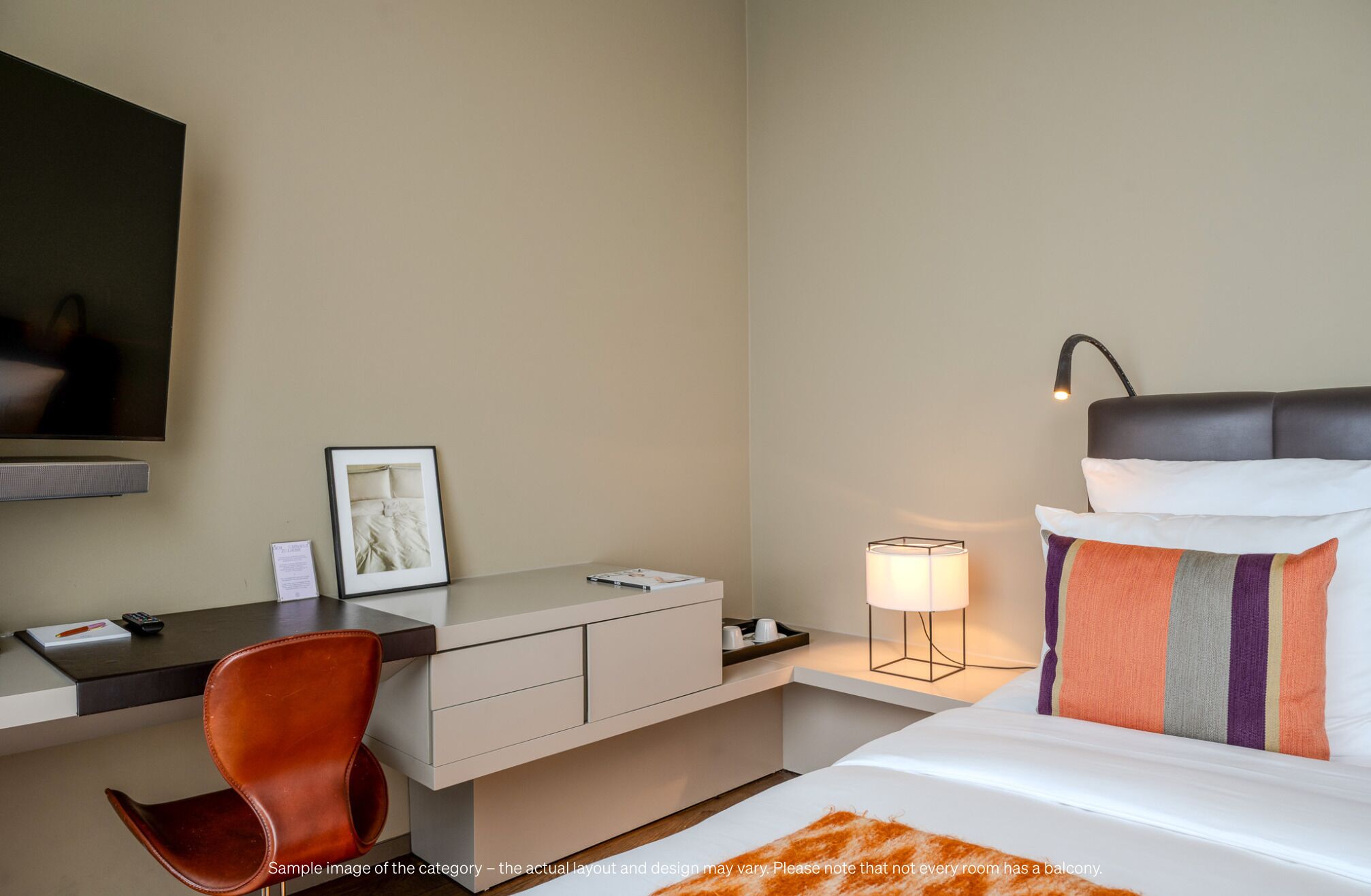 A hotel room with a bed, desk, chair, and a lamp.