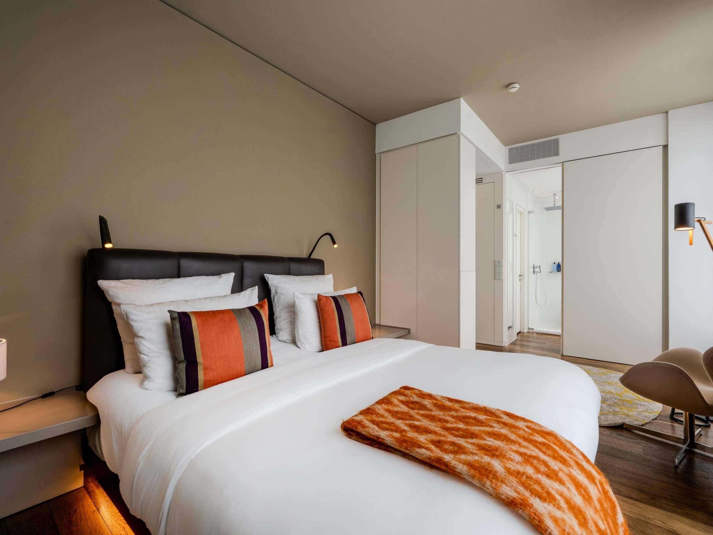A modern hotel room with a large bed, a bedside table, a chair, and a walk-in closet.