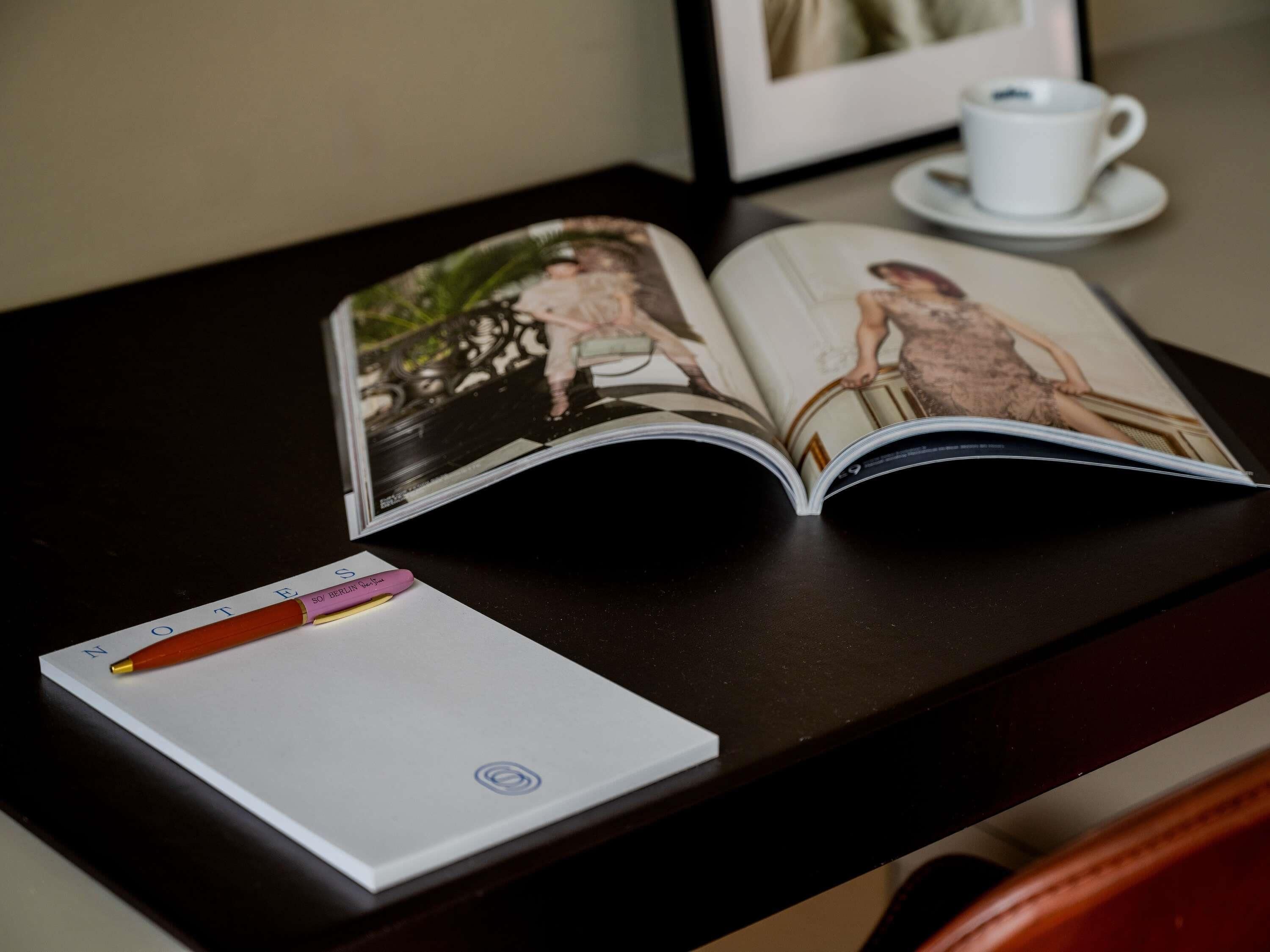 Ein Buch liegt auf einem Tisch, daneben ein Notizbuch mit Stift und eine Tasse.