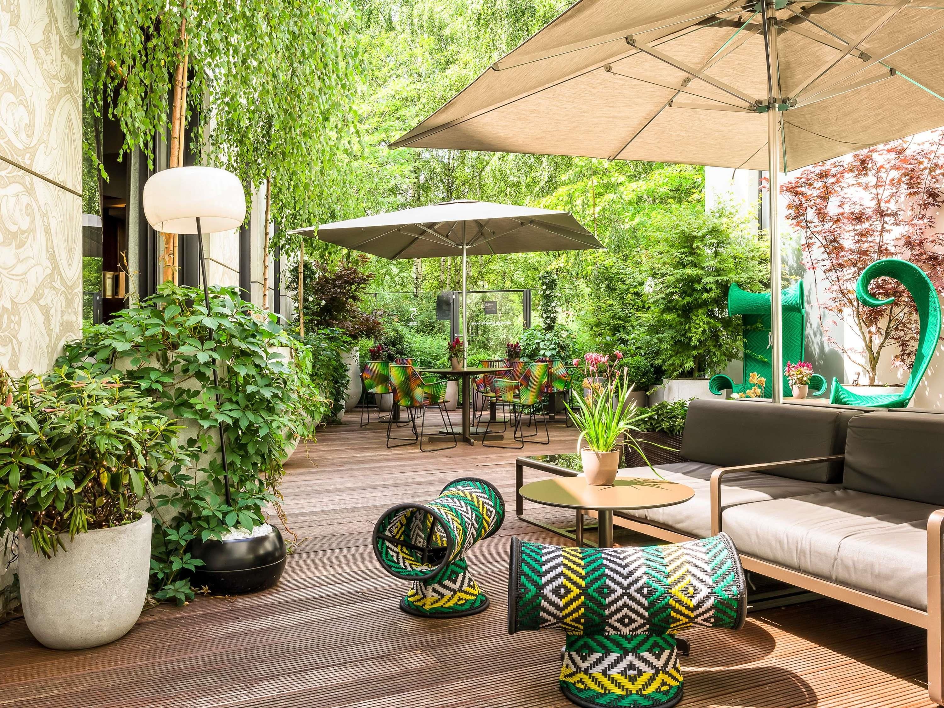 An outdoor seating area with tables, chairs, and umbrellas, surrounded by lush greenery and potted plants.