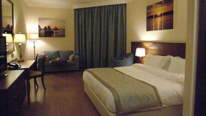 Una habitación de hotel con una cama, un escritorio con una silla, un sofá y un cuadro en la pared.