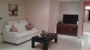 Una sala de estar con un sofá blanco, una mesa de centro, un televisor de pantalla plana y un mueble.