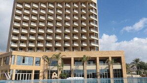 Un hotel moderno de gran altura con varios balcones, piscina y palmeras.