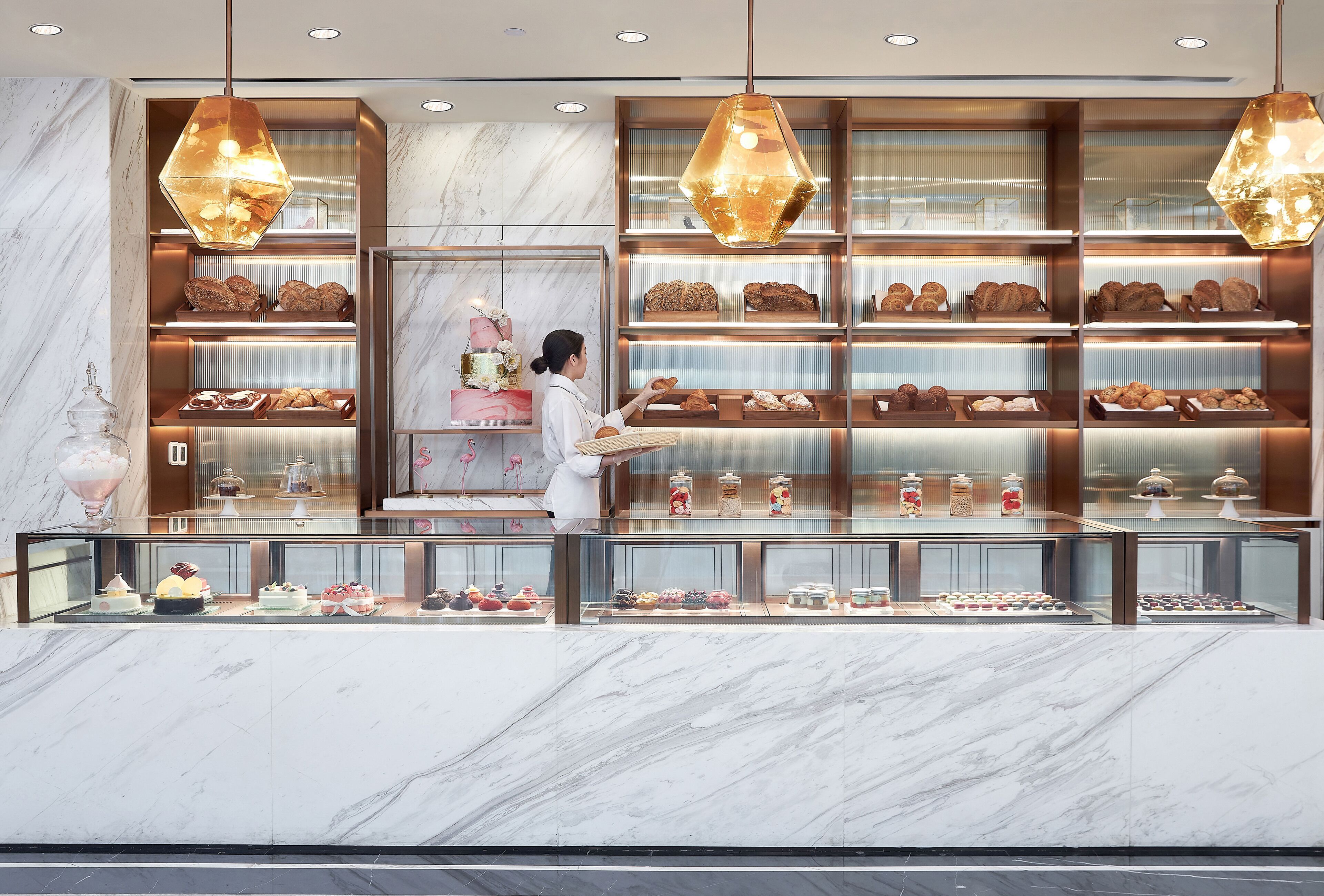 A bakery display with various baked goods and a person selecting a pastry.