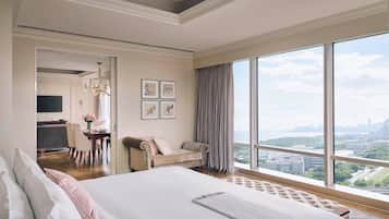 A spacious bedroom with a large bed, a desk with a chair, and a view of a cityscape through large windows.