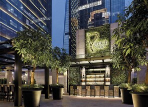 Un área de bar moderna con fachada de vidrio, plantas en macetas y diversas opciones de asiento.