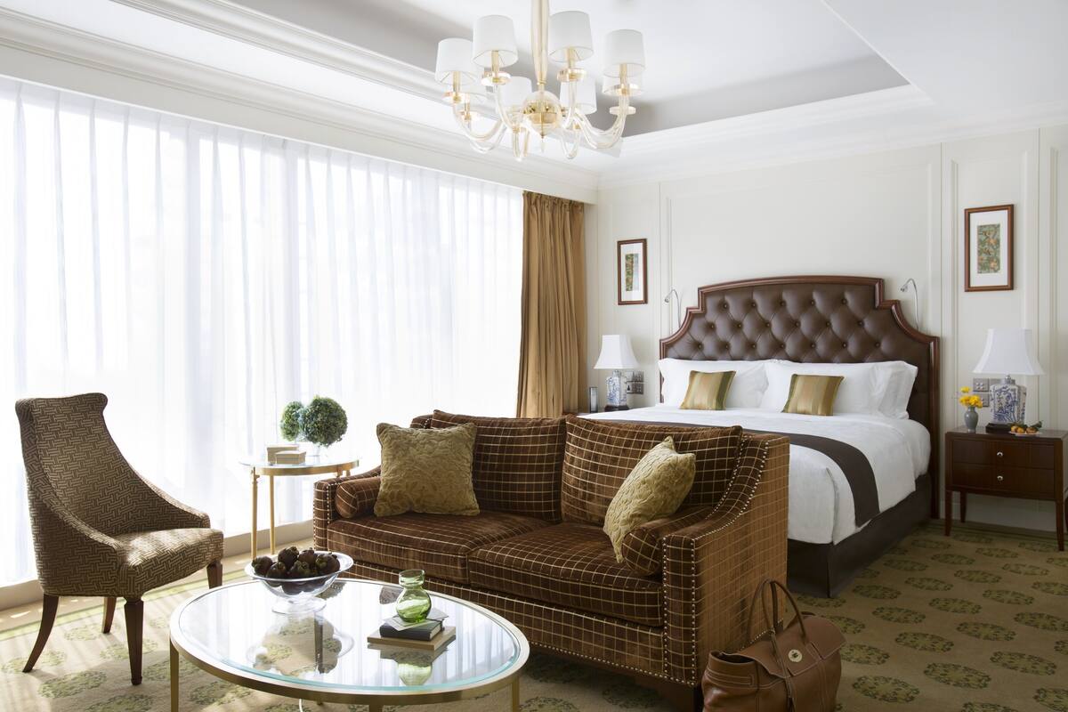 Ein Hotelzimmer mit einem großen Bett, einer braunen Couch, einem Glastisch und einem Sessel.