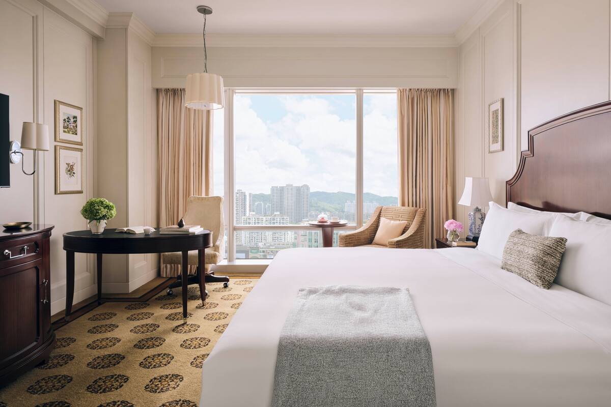 Ein Hotelzimmer mit einem großen Bett, einem Schreibtisch mit Stuhl, einem kleinen Tisch und Blick auf die Stadt.
