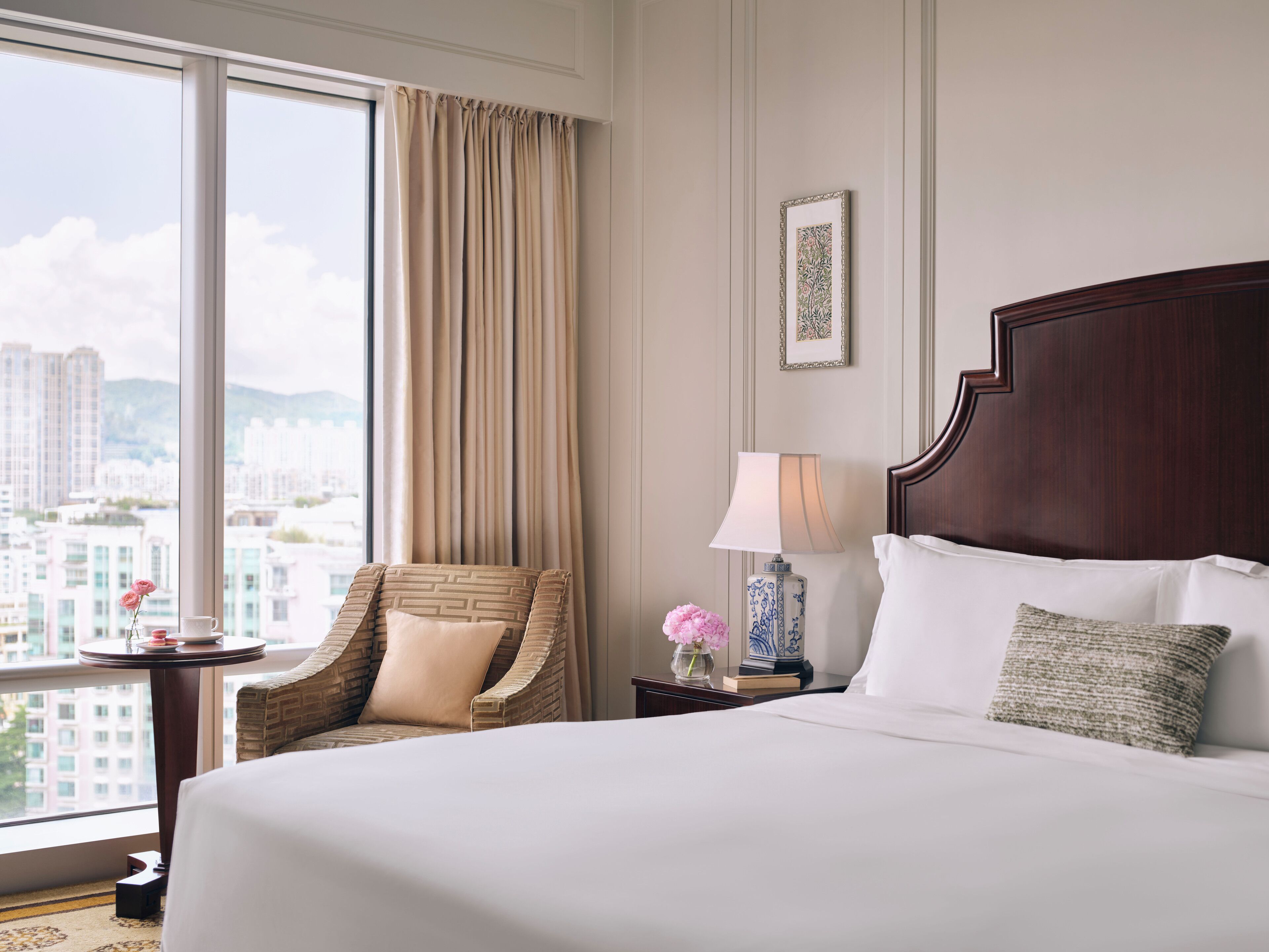 A hotel room with a large bed, a chair, a nightstand, and a window with a city view.